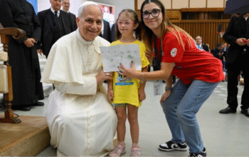 Pope Leo XIV bends down to take a photo with a girl taking part in the Vatican summer camp (@Vatican Media)