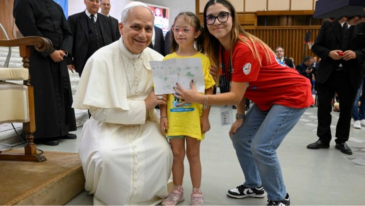 Pope Leo XIV bends down to take a photo with a girl taking part in the Vatican summer camp (@Vatican Media)